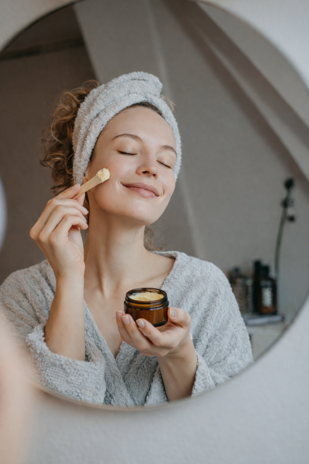 Woman applying cream to her face with a mirror reflection showing a skincare routine.