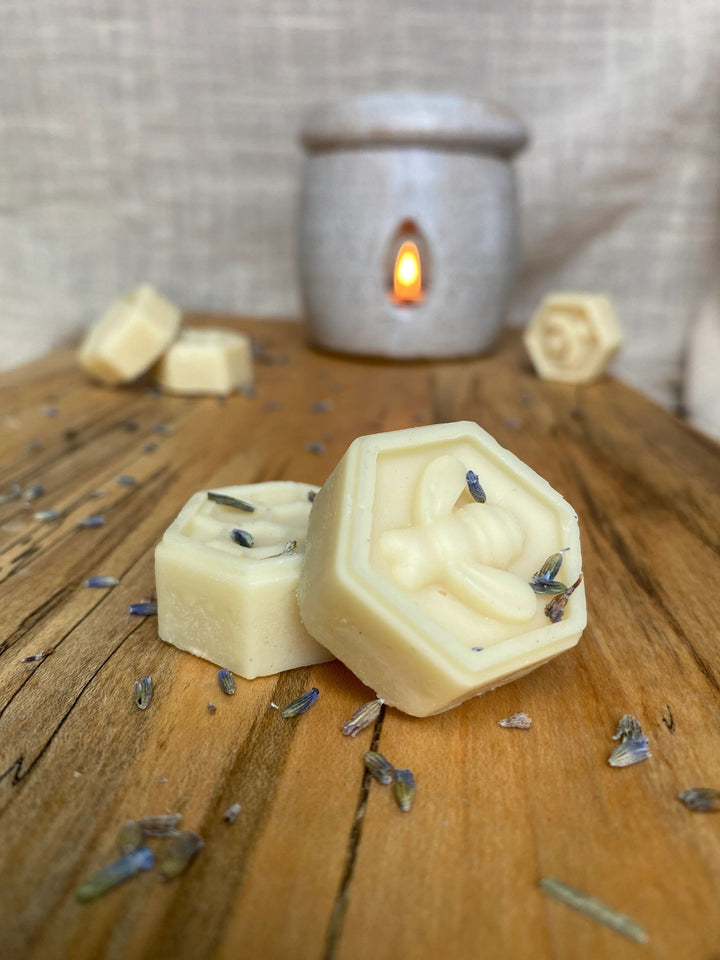 Hexagonal essential oil wax melts with lavender petals on a wooden surface with a lit candle in the background.