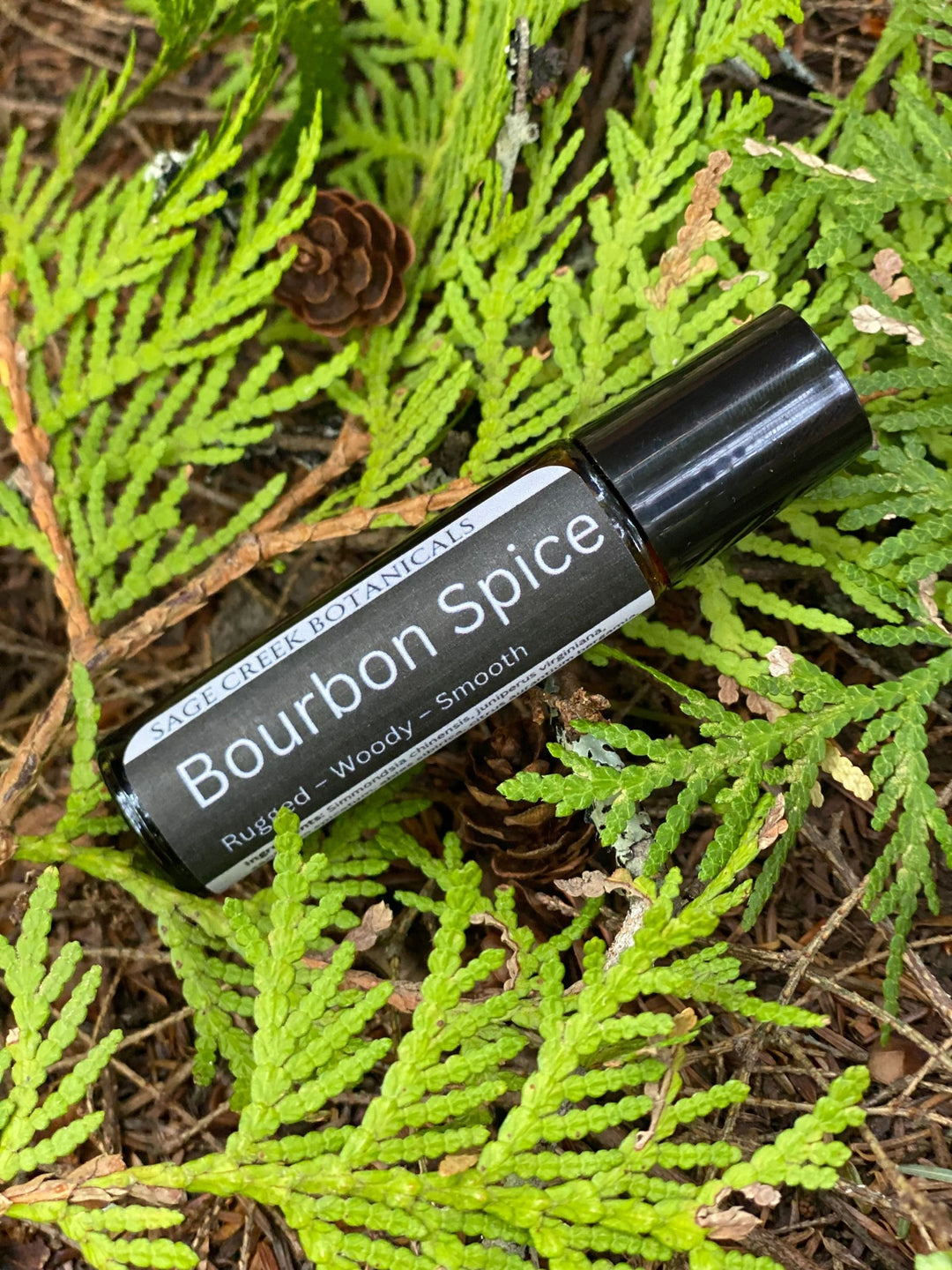 Roll-on bottle labeled 'Bourbon Spice' on a background of green foliage and pine cones.