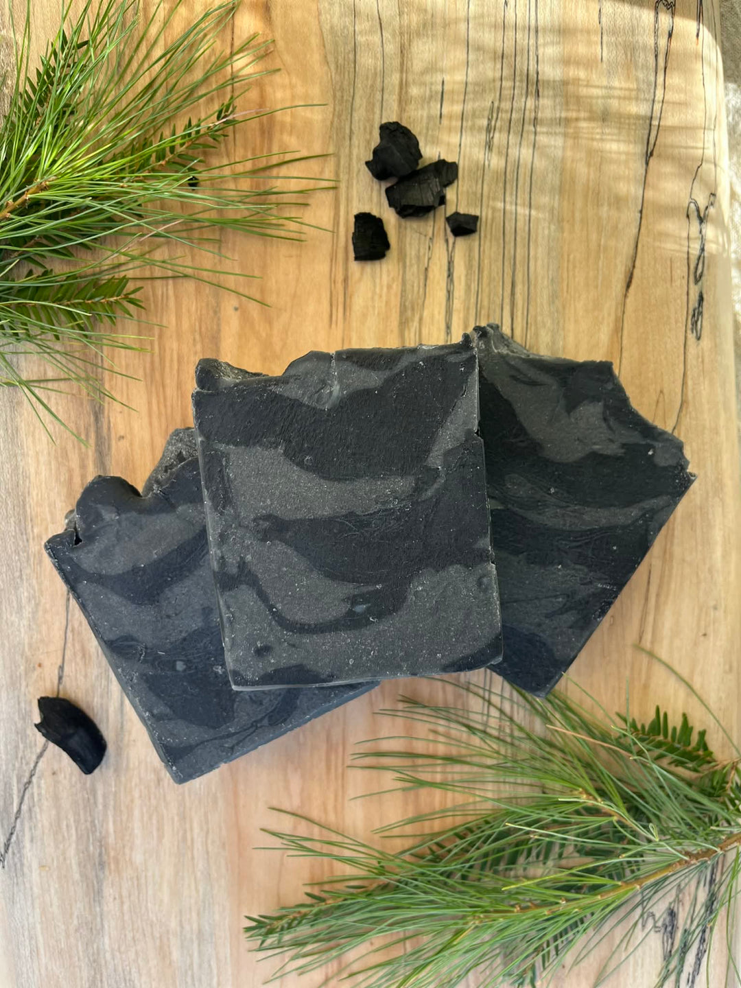 Black soap bars on a wooden surface with greenery and charcoal