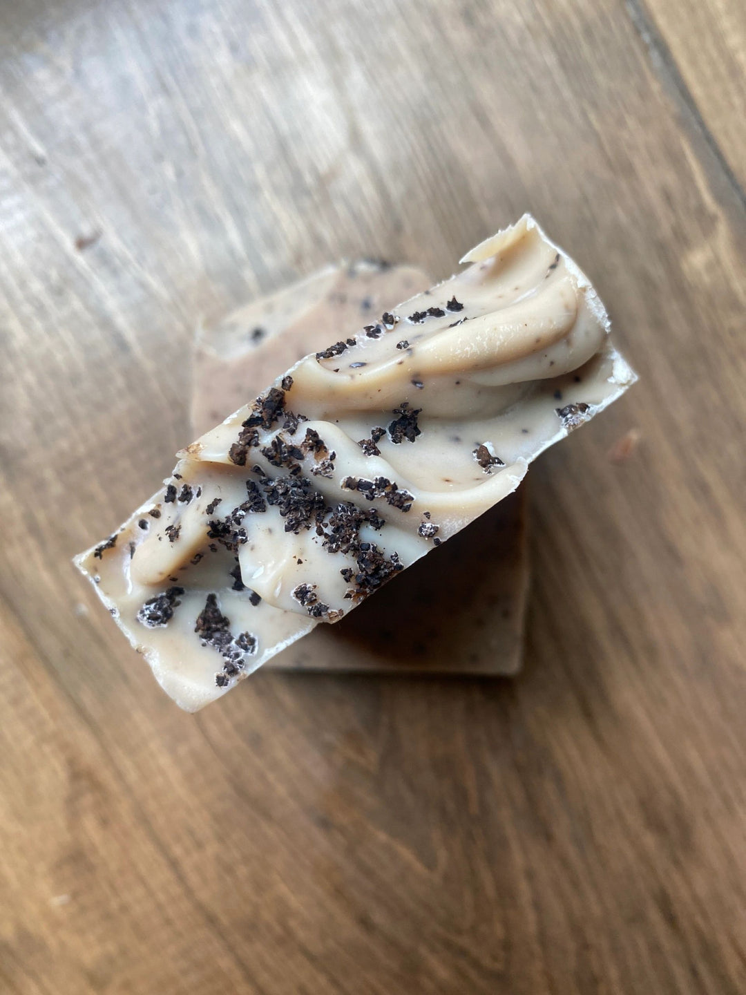 Sage Creek Botanicals Bar of soap with coffee sprinkled on top sitting on a wood surface