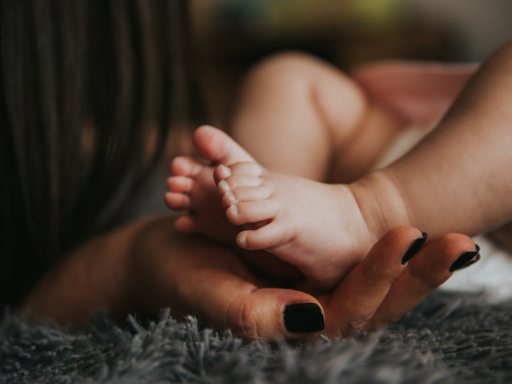 Close-up of a baby's foot held by an adult hand on a soft surface