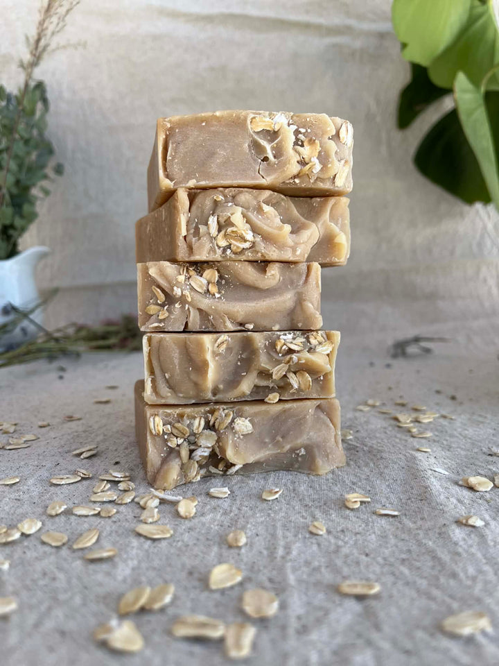Stack of Sage Creek Botanicals oats & Honey facial soap bars on a textured surface with scattered oats.