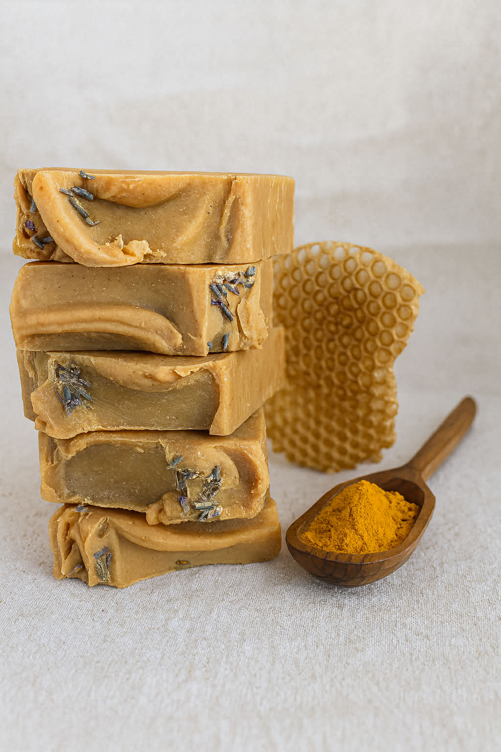 Stack of Sage Creek Botanicals facial soap bars with a wooden spoon of turmeric and a honeycomb on a linen